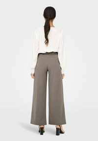 Mjuk vit blus i kombination med högmidjade, vida byxor i dämpad grå färg. Byxorna har en slät yta och elastisk midja. Svarta blockklack-sandaler.