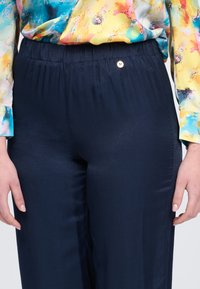 I pantaloni blu navy presentano un tessuto morbido e leggero con una cintura elastica e un piccolo dettaglio metallico nella parte anteriore.