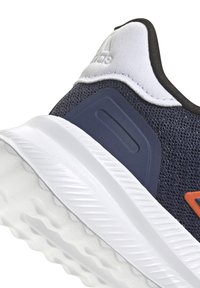 Zapatilla deportiva azul marino con parte superior de malla texturizada, acento blanco a lo largo de la suela, detalle del logo en naranja y collar acolchado para mayor comodidad.