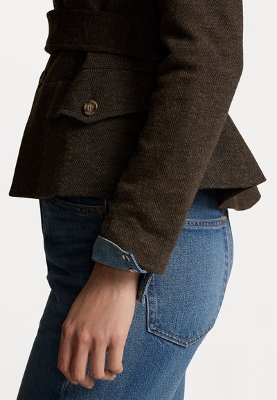Hnědý blazer s rybí kostrou a páskem v pase, spárovaný se světle modrými džíny s knoflíkovým manžetovým zakončením.