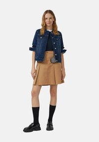 Jeansjack met een lichte wassing, zwarte top, tan kleurige geplooide rok, zwarte kniekousen en glanzende zwarte schoenen; verstelbare taille met een sierraad in dierenprint.
