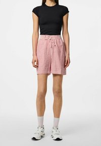 Černý přiléhavý top s krátkým rukávem v kombinaci s červeno-bílými pruhovanými šortkami s elastickým pasem a šňůrkou na stažení. Nošeno s bílými teniskami.