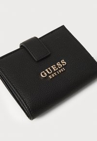 Portofel negru din piele texturată cu un logo auriu "GUESS EST1981" pe față. Dispune de o închidere cu clapetă și are o formă compactă, rectangulară.