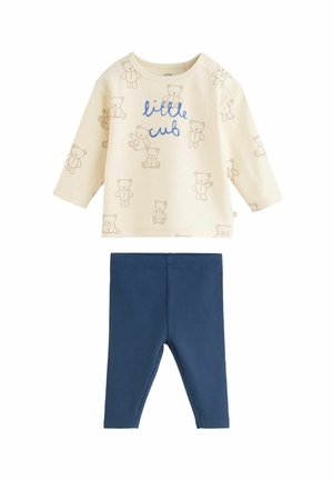 Kréme farbené tričko pre bábätká s dlhým rukávom s potlačou hnedých medvedíkov a textom "malé mláďa" v kombinácii s jednobarevnými modrými legínami pre bábätká.