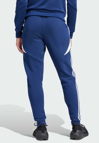 Marine joggers met witte zijaccenten, taps toelopende pasvorm, ribgebreide manchetten, gladde textuur, gedragen met zwarte sportschoenen.