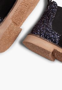 Botín de ante negro y purpurina morado oscuro, con una suela de goma texturizada color canela y paneles laterales elásticos para facilitar su uso.