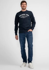 Námořnická mikina s bílým potiskem, kulatým výstřihem, žebrovanými manžetami a lemem, kombinovaná s modrými džínami a bílými teniskami. Hladká textura tkaniny.