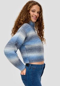 Blauer und grauer gestreifter, verkürzter Pullover mit einem hohen Hals, gestrickter Textur und langen Ärmeln, kombiniert mit blauen Jeans.