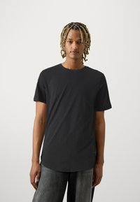 Sort, kortærmet t-shirt lavet af blødt bomuld, med rund halsudskæring og en let buet kant. Bæres sammen med løstsiddende, grå bukser.