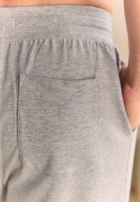 I joggers in cotone grigio presentano una vita elasticizzata e una tasca posteriore. Il tessuto ha una texture morbida con sottili variazioni di colore.