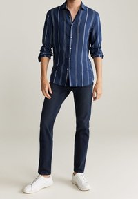 Námořnická pruhovaná košile s dlouhými rukávy, spárovaná s tmavými džíny a bílými teniskami. Košile má slim fit střih a lehký materiál.