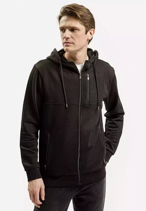 Czarna bluza z kapturem na zamek, wykonana z miękkiego materiału, z przednią kieszenią, kapturem na sznurku i dopasowanym krojem. Widoczne teksturowane akcenty na ramionach.