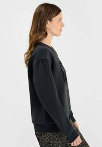Svart tröja med ribbad mudd och nederkant, har en rund halsringning. Modellen bär den med mönstrade, smalrandiga byxor.