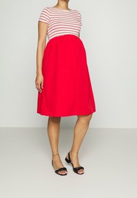 Röd klänning med en randig, kortärmad topp. Bodicen är figurnära, och går över till enLoose kjol som slutar precis ovanför knäet. Svarta sandaler.