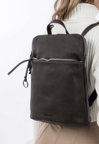 Hnědý kožený batoh s texturovaným povrchem, s uzávěrem na zip, přední kapsou a nastavitelnými popruhy. Obsahuje horní ucho a stříbrné kovové prvky.