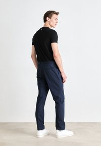 Navy trousers in a tailored fit with side and back pockets, paired with a fitted black t-shirt and white sneakers. Smooth texture.
