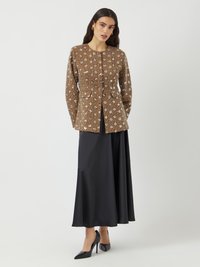 Veste à motifs floraux brun avec un col rond, fermeture à boutons et design peplum, associée à une longue jupe noire et des escarpins pointus.