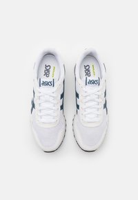 White athletic shoes with a mesh upper, navy blue accents, and black rubber sole. Features include a padded collar and laces.