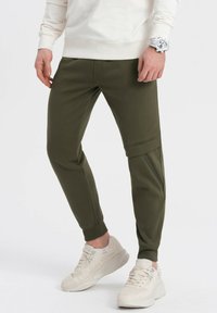 Olivově zelené tepláky z měkké tkaniny, s tapered designem, manžetami na zápěstí a detaily se zipovou kapsou na boku.