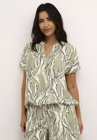 Chemise ample à manches courtes en lin vert clair avec un motif marbré noir et blanc. Présente un col en V et un design décontracté.