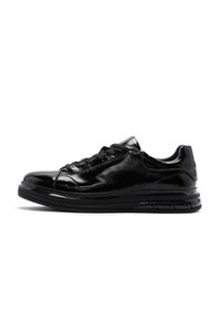 Zapatilla deportiva negra con acabado brillante, puntera redondeada, diseño con cordones, suela acolchada y un patrón de relieve distintivo para un mejor agarre.