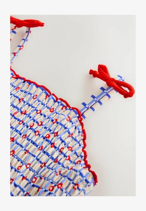 Haut smocké avec motif rayé rouge et bleu, présentant des accents rouges et des liens, fabriqué en tissu léger avec une finition texturée.