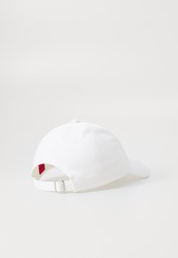 Cappellino da baseball bianco con strap regolabile, realizzato in tessuto con una superficie liscia. Etichetta rossa visibile sul retro, design con visiera curva.