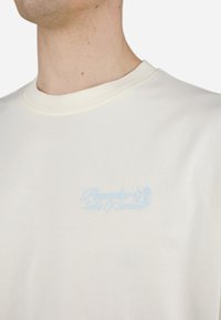 Bílý bavlněný tričko s kulatým výstřihem. Obsahuje světle modrý textový design "Paradiso Scent of Summer" na levé části hrudi.