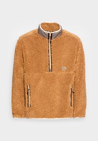Pullover in pile color cammello con mezza zip frontale, colletto rialzato, due tasche con zip e una piccola patch rettangolare con logo sul petto.