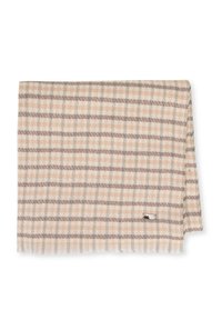 Couverture tissée légère avec un motif à carreaux beige, gris et bleu clair. Elle présente une frange subtile et une petite étiquette métallique avec logo.