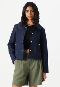 Veste en jean foncé avec un grand col, des boutons-pression et deux poches avant. Présente des coutures contrastées et un design court.