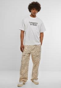 White cotton t-shirt with "Contemporary Art Market" printed in black. Beige pants with a topographic pattern and multiple pockets. Cream sneakers.