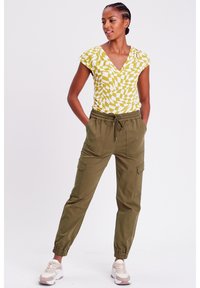 Top a V con scollo a V giallo e bianco a fantasia abbinato a pantaloni cargo verdi. I pantaloni hanno polsini elasticizzati e tasche. Sneakers di colori chiari completano l'outfit.