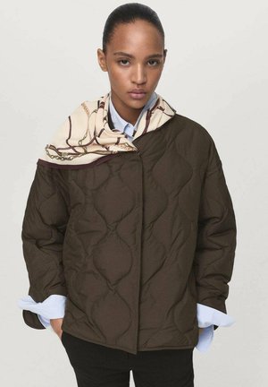 Chaqueta marrón acolchada con un cuello alto, llevada sobre una camisa azul claro, combinada con una bufanda crema con estampado alrededor del cuello.
