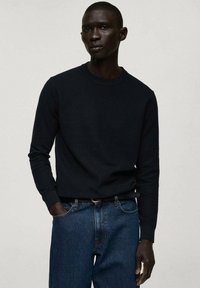 Pulover lung cu mânecă lungă, de culoare bleumarin închis, cu guler rotund, textură ribitată, asortat cu blugi de denim de culoare albastru deschis. Design simplu, fără modele vizibile.