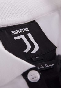 Witte polo met een zwart label waarop "JUVENTUS" in witte letters staat en een logo-ontwerp heeft, met een knoopsluiting. Maatlabel "S."