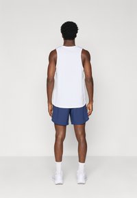 Λευκή αμάνικη αθλητική μπλούζα και ναυτικές σορτς, με χαλαρή εφαρμογή και μαλακό ύφασμα. Λευκά αθλητικά παπούτσια και κάλτσες μέχρι τον αστράγαλο ολοκληρώνουν την εμφάνιση.