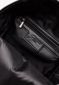 Interno della borsa nera con fodera in tessuto liscio, tasca con zip, etichetta logo in rilievo e dettagli hardware della zip eleganti.
