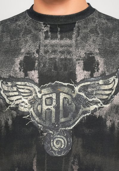 Close-up of a dark, worn T-shirt with a faded winged emblem and letters "RC" centered on the chest.