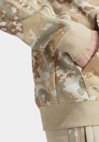 Sudadera con estampado de camuflaje en beige, verde y crema; cuenta con puños de canalé y un corte relajado con un bolsillo tipo canguro.