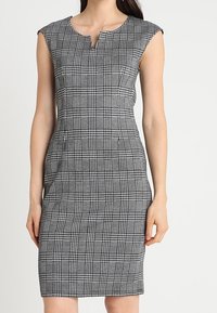 Robe grise à carreaux avec une silhouette crayon, manches courtes, coupe mi-genou, dotée d'un décolleté en V et de poches latérales. Tissu tissé texturé.