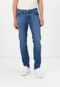 Sinine last denim teksad, kitsas lõige, viie taskuga disain ja nööp kinnitusega. Kandmine valgete tossudega kontrasti loomiseks.
