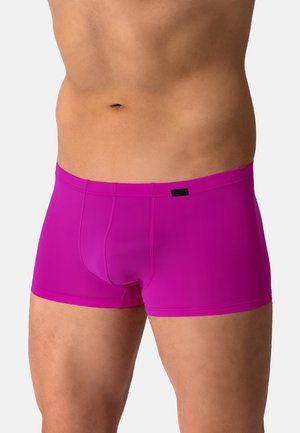 Mannelijke torso die felroze nauwsluitende boxershorts draagt tegen een effen lichte achtergrond.