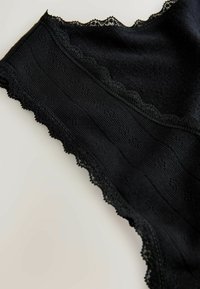 Black seamless knit underwear with lace trim and subtle floral patterns on a plain light background.