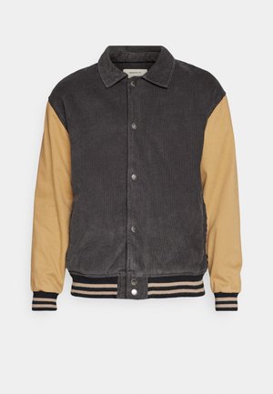 Corduroy and smooth fabric jacket with a dark gray body and tan sleeves. Features snap buttons and striped ribbed cuffs and hem.