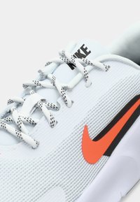 Lyseblå sportssko med tekstiloverdel, hvide snørebånd, sort og orange Nike-logo, struktureret design og polstret krave.