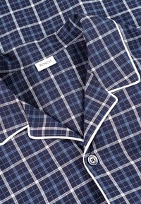 Chemise de pyjama à carreaux bleu marine avec passepoil blanc, présentant un col classique et une fermeture à boutons, étiquetée avec la marque "RÖSCH."