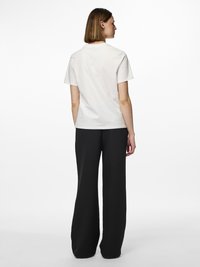 T-shirt blanc en coton à manches courtes vu de dos, associé à un pantalon noir à jambes larges, avec une coupe décontractée et un col rond.