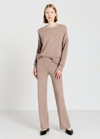Beige Strickpullover und passende Hose, beide mit einem lässigen Schnitt. Der Pullover hat einen runden Halsausschnitt und einen gerippten Abschluss; die Hose hat eine glatte Textur.