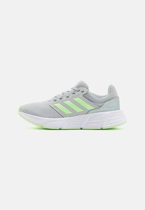 Gray athletic shoe with mesh upper, green accents, and three stripe logo. Features a white sole with green detailing and a padded collar.